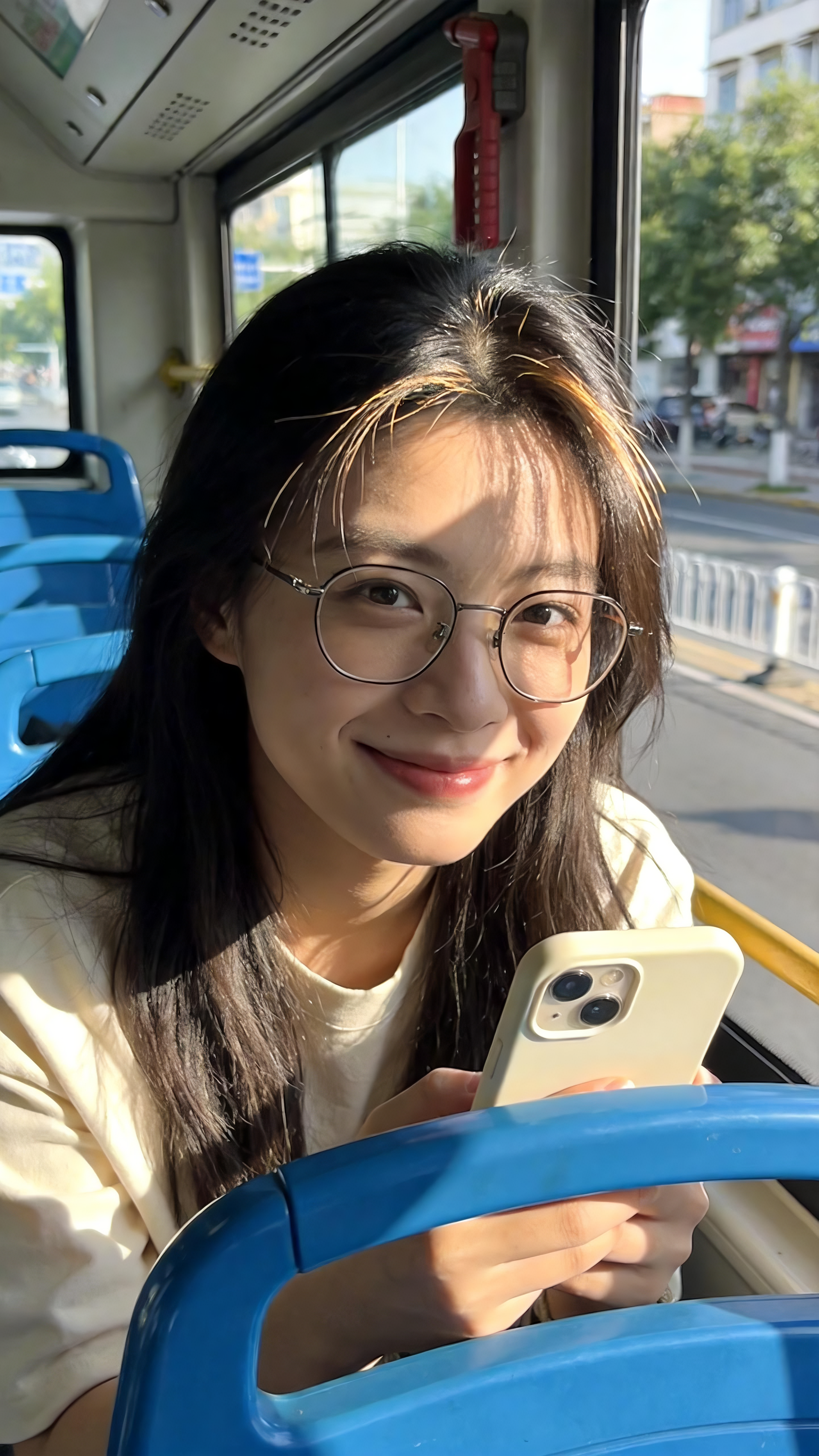 生成内容提示词：公交车内场景，年轻女性，浅色上衣，佩戴眼镜，手持米白色手机，蓝色公交座椅，窗外有街道、树木、建筑。 阴影光线细节提示词：阳光透过车窗洒入，阳光透过发丝照到身上，形成明亮的光影效果，人物头发和身上有阳光照… - AI提示词参考图，来自西西提示词