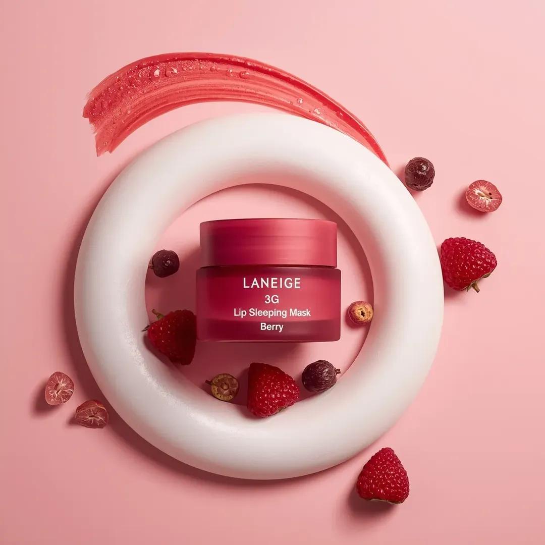 A centrally placed pink cosmetic jar labeled “LANEIGE Lip Sleeping Mask [Berry] 3 g” sits on top of a large s… - AI提示词参考图，来自西西提示词