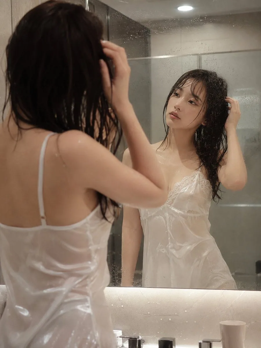 一名23歲日系女性，穿著微濕的白色細肩帶絲綢睡衣。她站在充滿水氣的浴室鏡子前，正隨意整理著微濕的頭髮。水氣讓輕薄的絲綢布料微微貼合在優美的身體曲線上，在浴室柔和的頂光下散發著細膩的光澤與微透感，慵懶且私密，不暴露敏感部… - AI提示词参考图，来自西西提示词