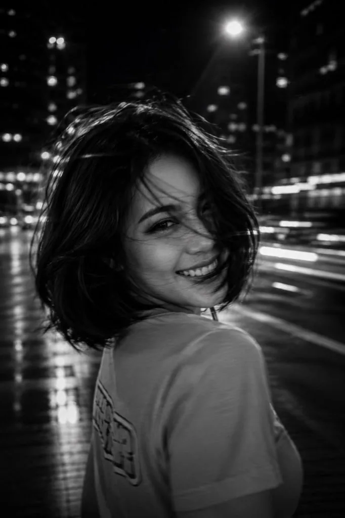 A black-and-white cinematic photograph of a young woman at night in the city, shot with a long exposure and i… - AI提示词参考图，来自西西提示词