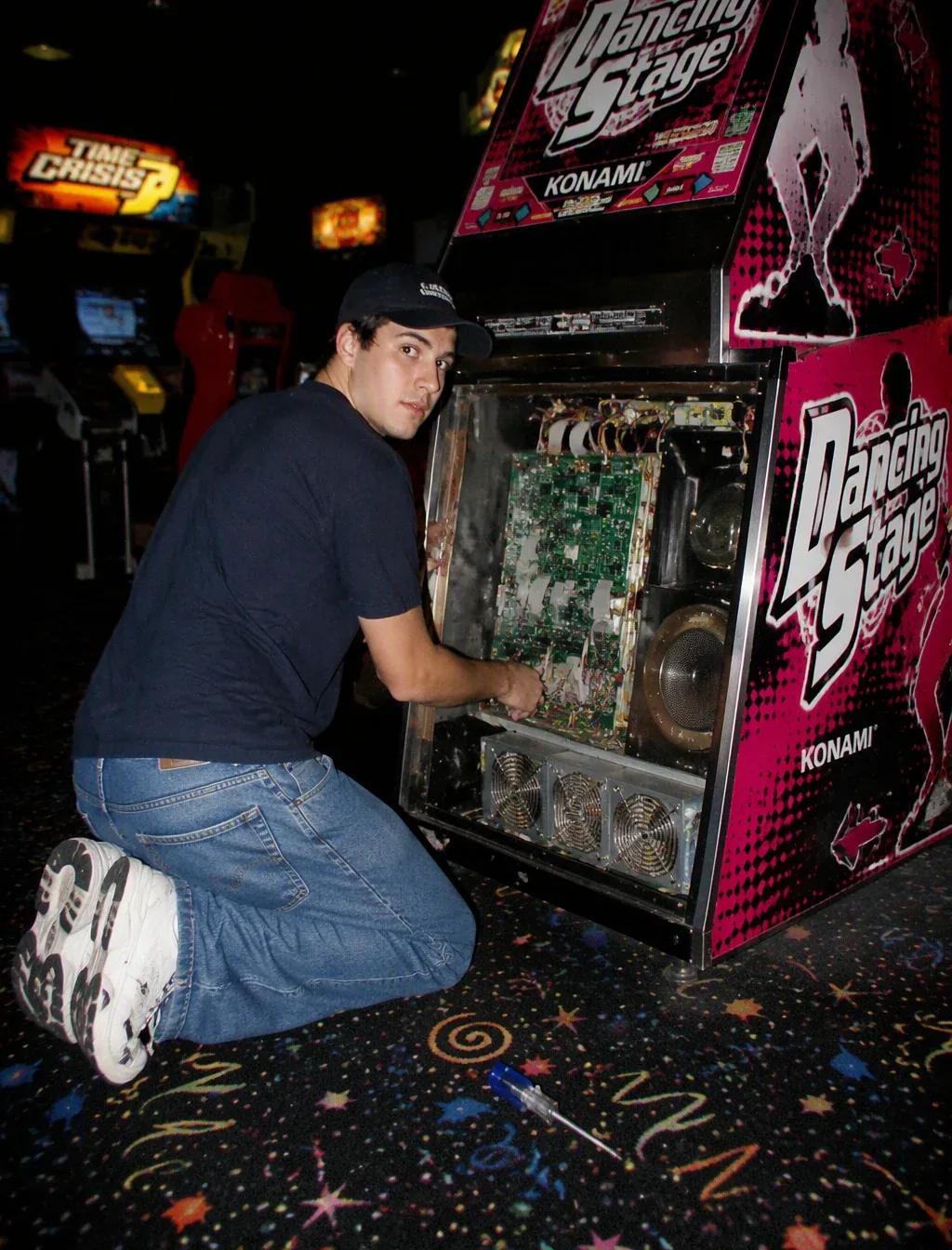 A vintage, late 90s amateur flash photograph of a young man repairing an arcade machine. He is kneeling on a … - AI prompt reference from CC Prompt Galaxy