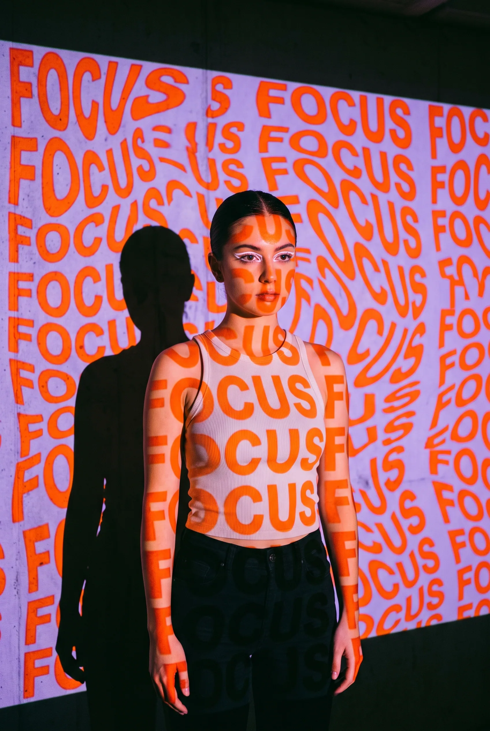 A young woman stands in front of a wall with a projection of the word "FOCUS" repeated in a distorted, wavy p… - AI提示词参考图，来自西西提示词