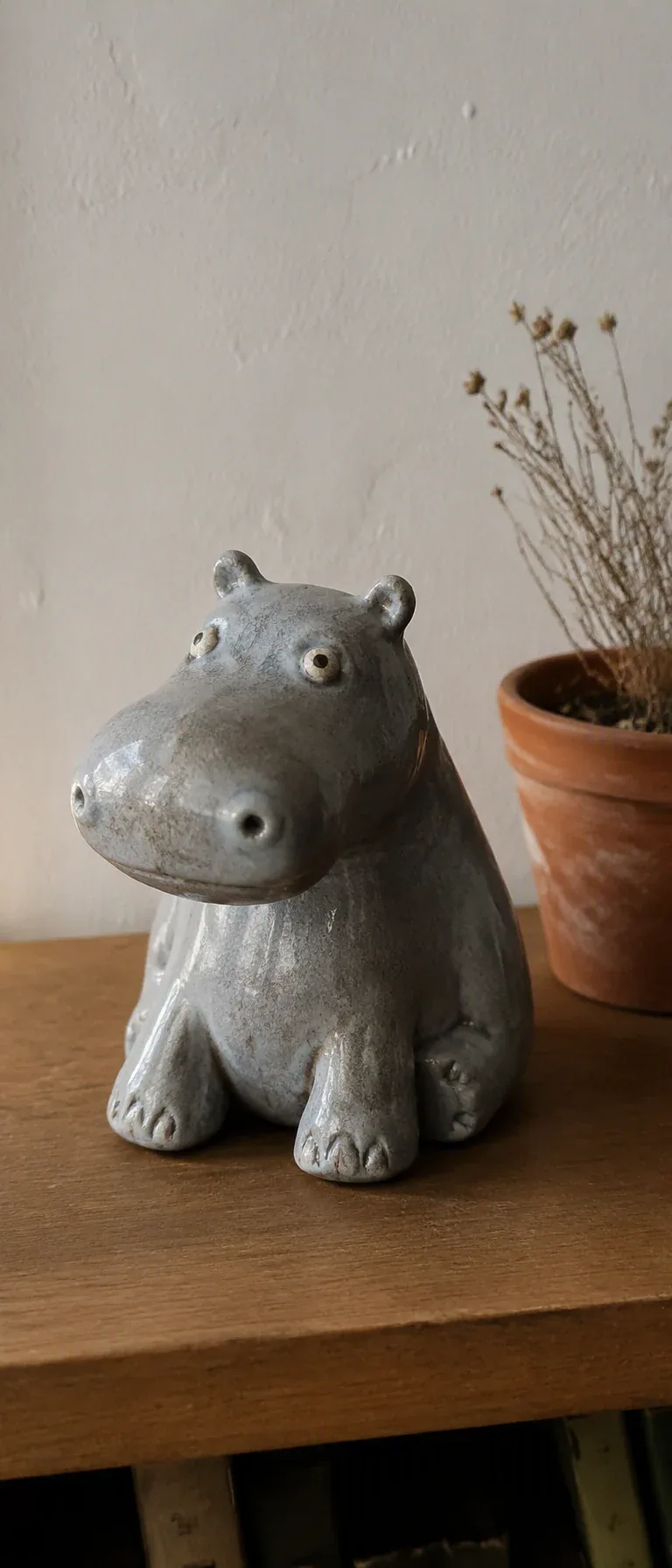 A vertical 9:20 photograph of a handmade ceramic hippopotamus figurine sitting on a wooden shelf.The figurine… - AI prompt reference from CC Prompt Galaxy