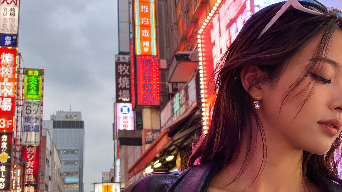 Create a photorealistic cinematic street portrait in a busy Japanese nightlife district at dusk. The frame is… - AI提示词参考图，来自西西提示词
